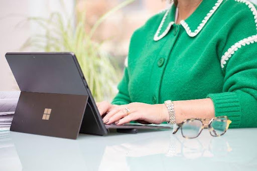 Person typing on tablet, wearing green sweater.