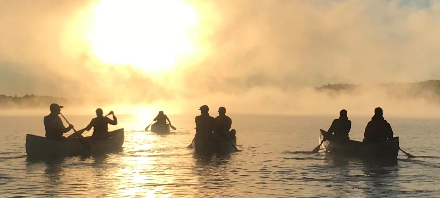 Canoeing at sunrise on misty lake.