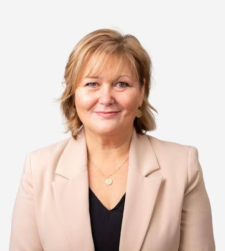 Smiling woman in beige blazer, neutral background.