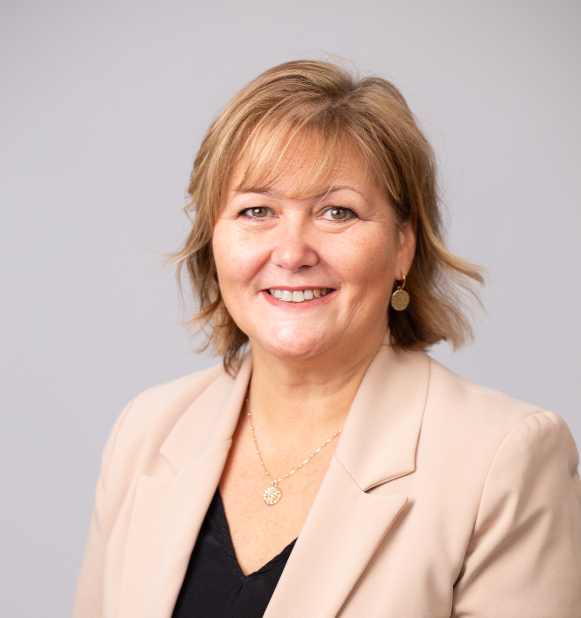 Smiling woman in beige blazer, neutral background.
