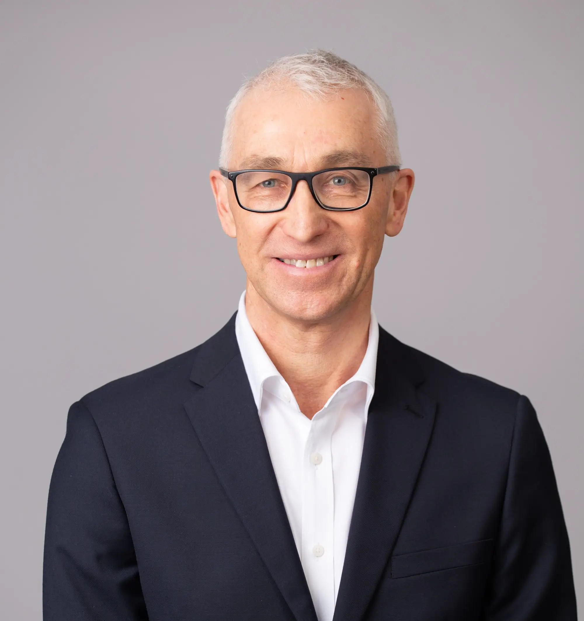 Man in suit and glasses smiling confidently.